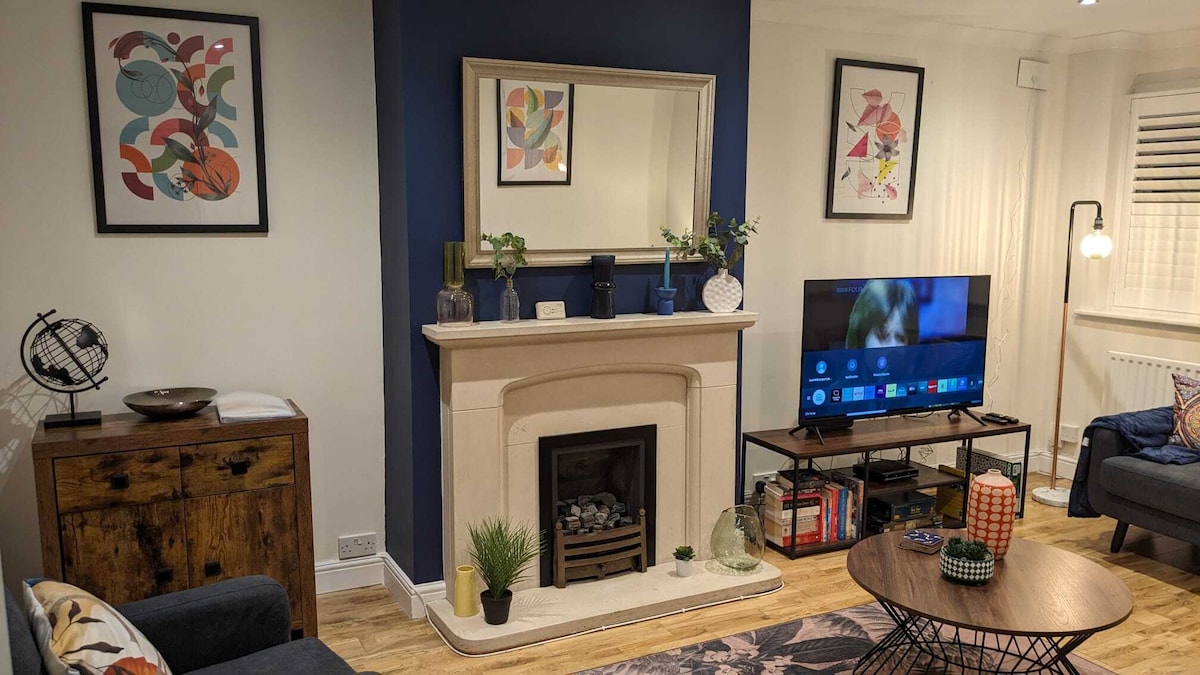 A cozy family room features a decorative fireplace flanked by modern artwork. A flat-screen TV is positioned on a light wooden entertainment unit. Comfortable seating is provided by soft sofas, and a round coffee table is displayed in the center, enhancing the inviting atmosphere.