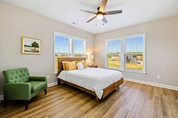 Bright bedroom with a queen-size bed, ceiling fan, and large windows providing natural light