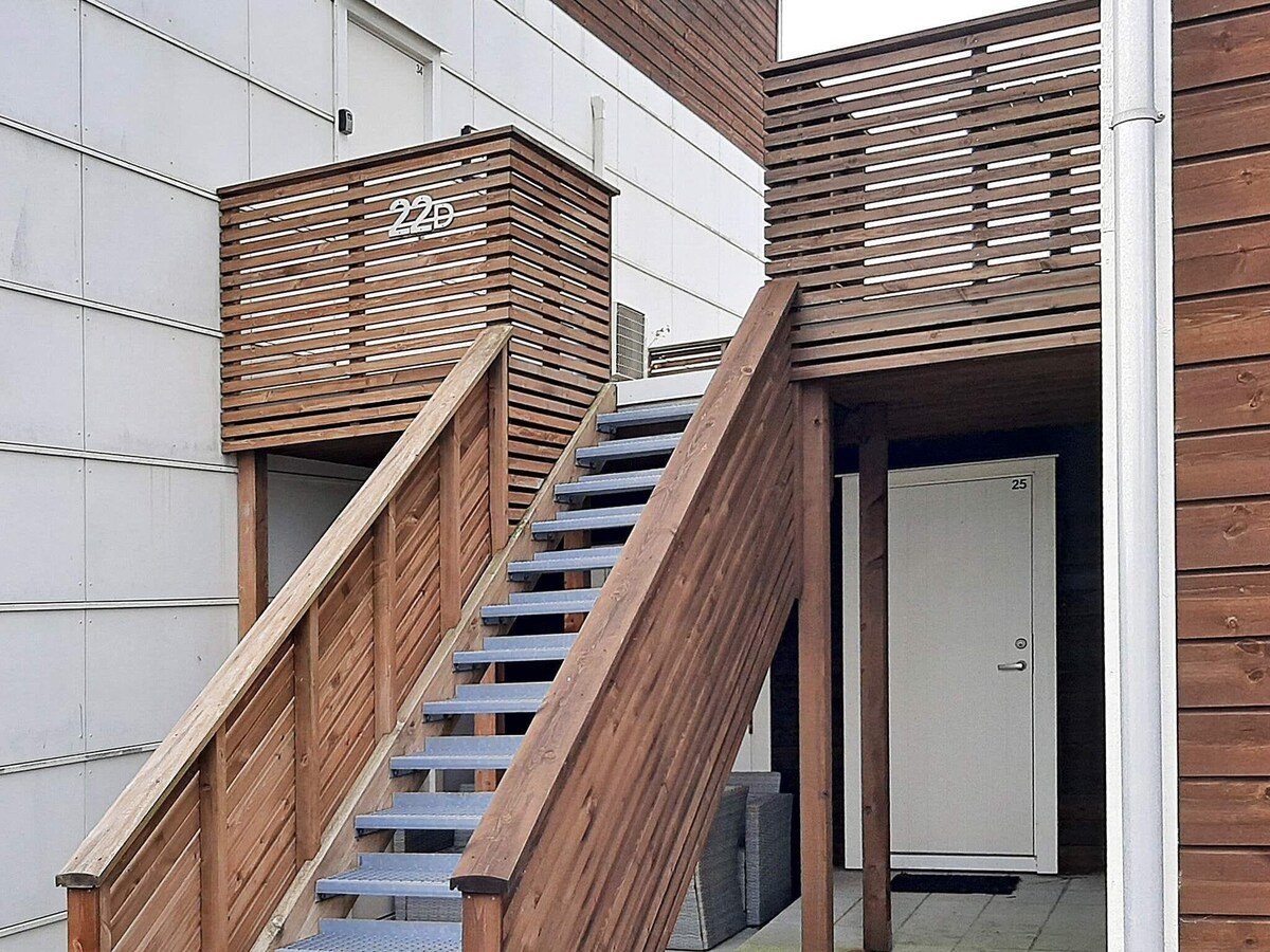 An outdoor staircase made of wood leads to elevated entrances, featuring a handrail for safety. The design includes wooden slats, providing a modern appearance. A white door is visible at the top, with the number 22D clearly displayed.