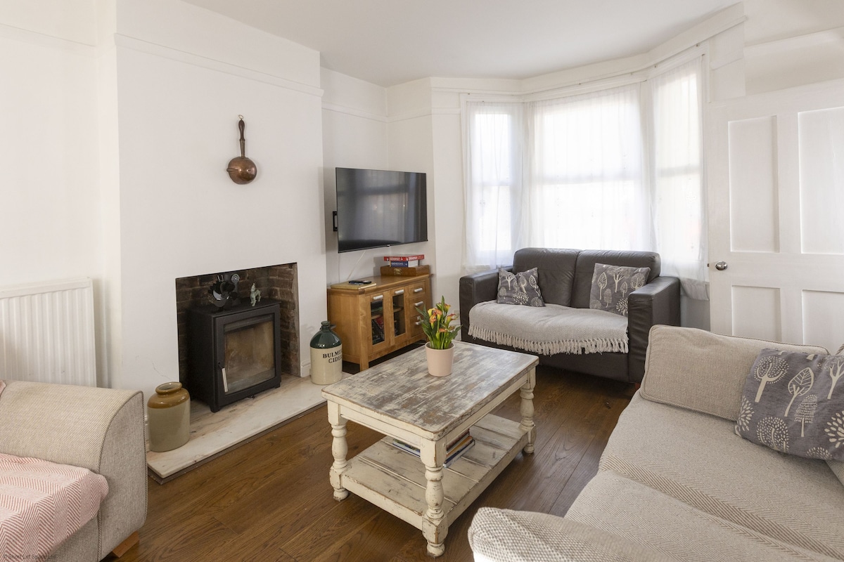 The bright lounge features comfortable sofas in neutral tones, complemented by a wooden coffee table at the center. A flat-screen Smart TV is mounted on the wall opposite the seating area. Sunlight filters through the large windows, creating a warm and inviting environment.