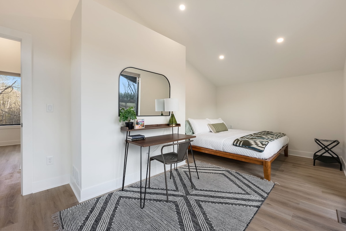 غرفة نوم واسعة مع سرير كينج، رف للأمتعة، مكتب، نوافذ XL مع إضاءة طبيعية وستائر تعتيم للغرفة. 