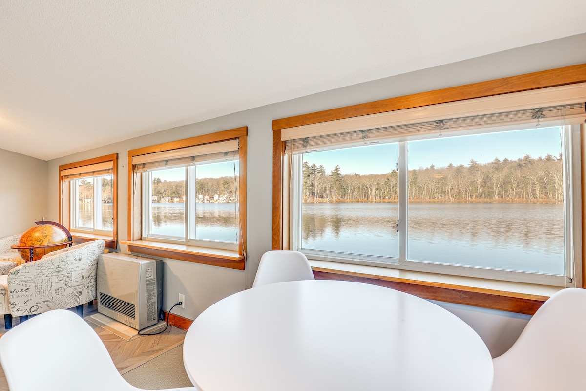 A dining area is featured beside large windows that offer views of Shadow Lake. Natural light fills the space, illuminating the simple round table surrounded by white chairs. A comfortable chair is positioned nearby, enhancing the inviting lakefront atmosphere.