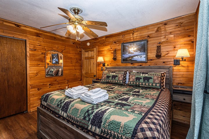 Cozy queen bedroom featuring warm wood paneling, nightstands, and soft lighting.