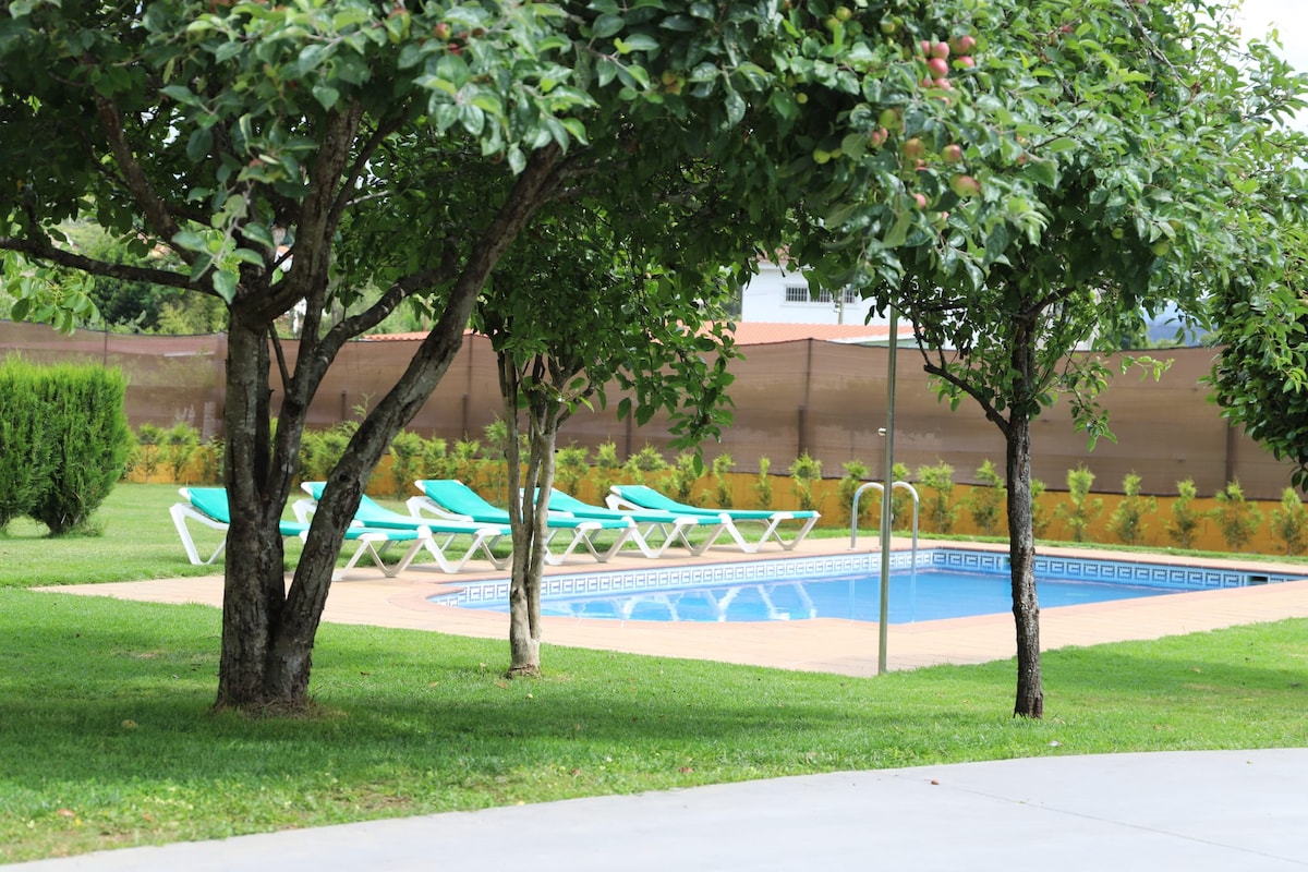 A refreshing swimming pool is surrounded by well-maintained grass and trees. Several sun loungers are positioned near the pool, offering a place to relax in the sun. The area is neatly landscaped, creating a peaceful outdoor environment.