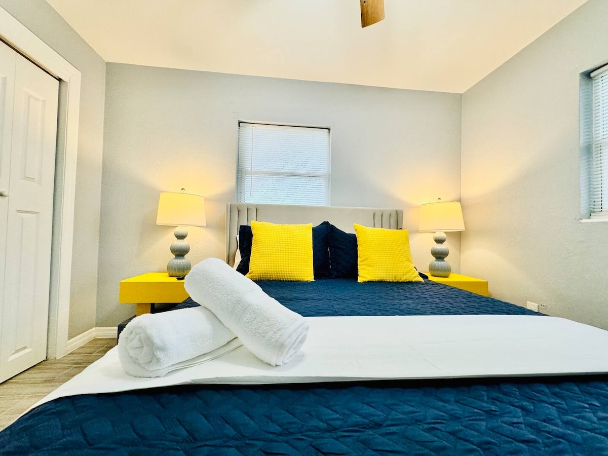 Camera da letto moderna a Lakeland, in Florida, negli Stati Uniti! Dispone di un letto accogliente con biancheria da letto blu navy, cuscini gialli vivaci, comodini abbinati e illuminazione calda. Perfetto per relax e stile.