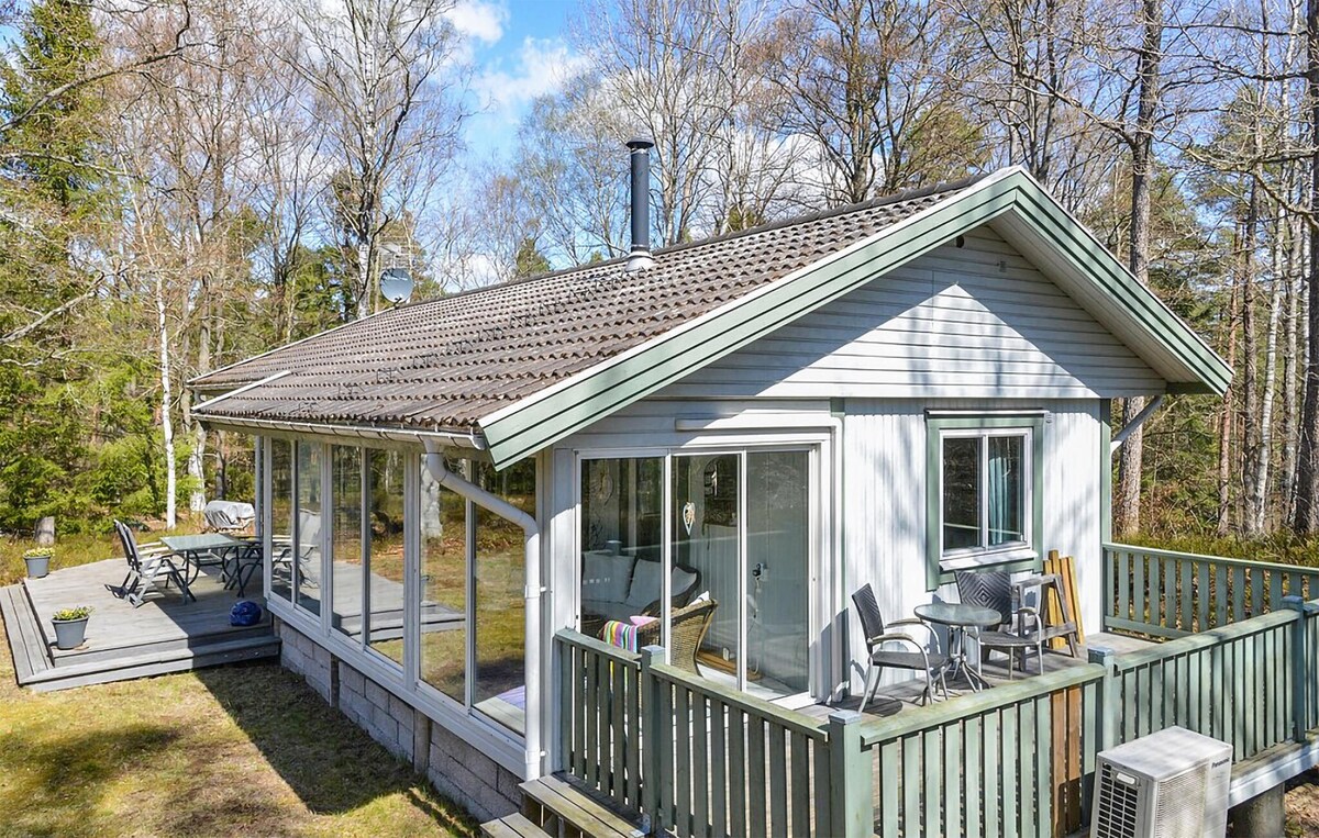 The exterior of the vacation home showcases a casual wooden design with large windows that offer views of the surrounding forest. A spacious terrace is furnished with a dining table and chairs, providing an inviting space for outdoor relaxation.