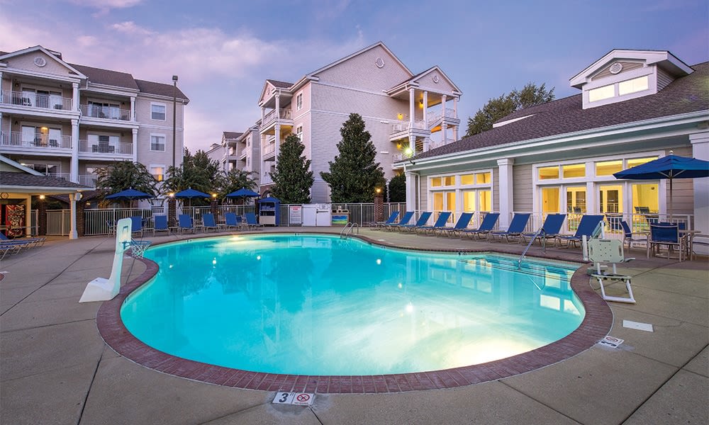 An outdoor swimming pool is surrounded by lounge chairs and umbrellas, creating a relaxed environment for guests. The pool is well-lit in the evening, with the resort buildings visible in the background, showcasing a blend of elegant architecture and landscaped greenery.