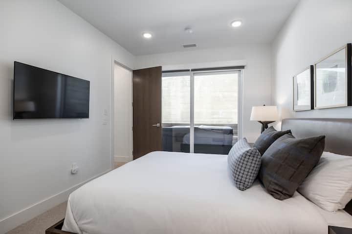 - Dormitorio con cama tamaño queen, cabecero acolchado y almohadas elegantes  
- TV de pantalla plana montada para el entretenimiento y noches de descanso  
- Ventana grande y puerta corredera con luz natural y vistas a la bañera de hidromasaje.