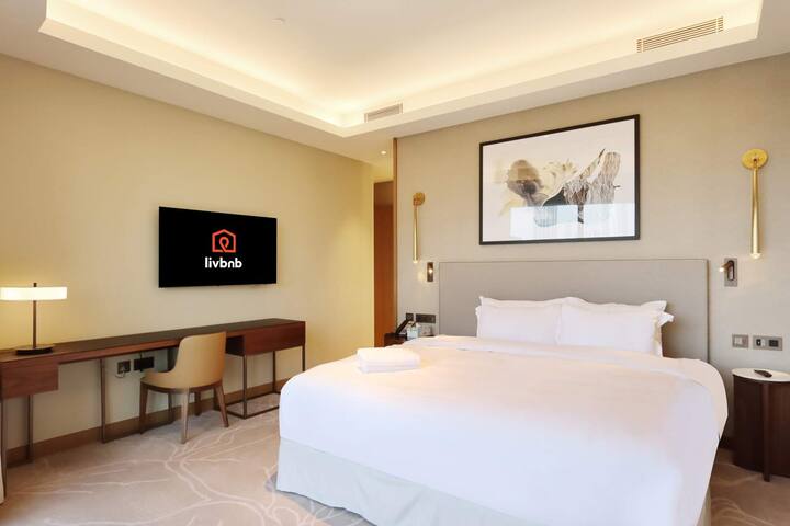 غرفة نوم رئيسية واسعة مع سرير كينج وإضاءة دافئة ومساحة عمل مخصصة.