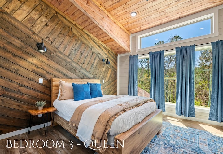 Unwind in comfort in this queen bedroom featuring a wooden accent wall, high ceilings with skylights, and plush bedding!