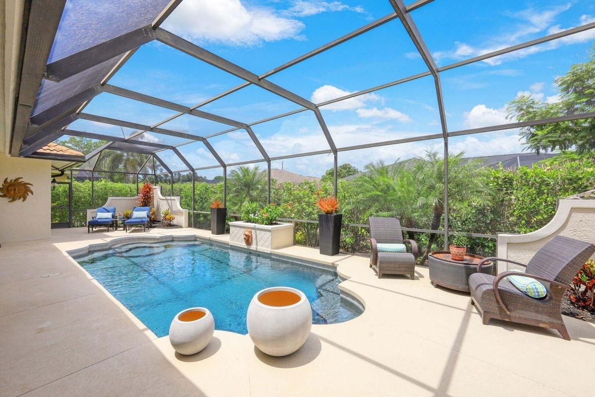 An outdoor space features a private pool framed by a screened enclosure that allows natural light in. Comfortable lounge chairs and a seating area provide options for relaxation, while potted plants add greenery to the tranquil environment.