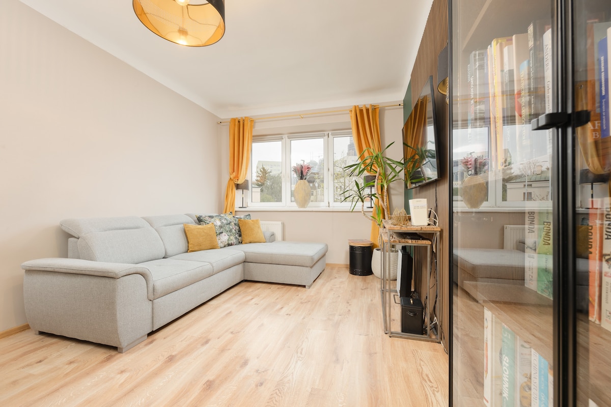 Una sala de estar luminosa y abierta con un sofá beige y una decoración elegante, con un gran espejo y detalles en tonos de madera.