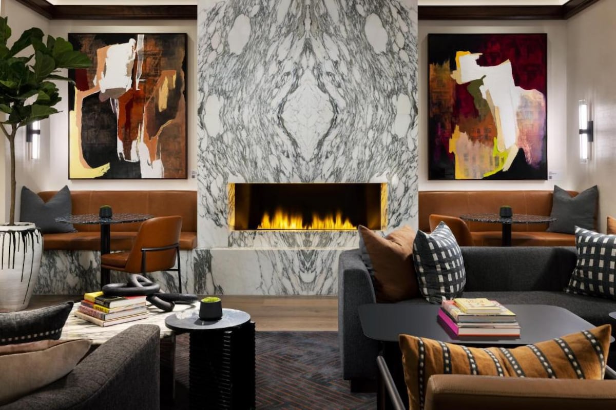 A stylish lounge area features a contemporary marble wall, framed by two abstract artworks. Comfortable seating arrangements include leather and fabric sofas, complemented by a modern fireplace that exudes warmth. Stylish lighting and decorative elements create an inviting ambiance for relaxation.