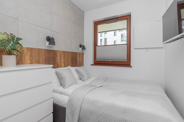 Otra habitación con una cama doble, ropa de cama blanca, una planta y un espejo sobre una cómoda.