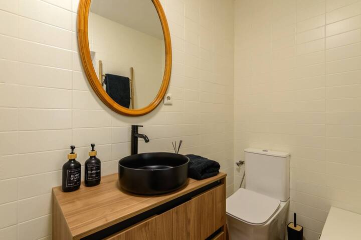 Baño con lavabo negro sobre madera y espejo circular dorado: detalles de diseño en cada rincón.