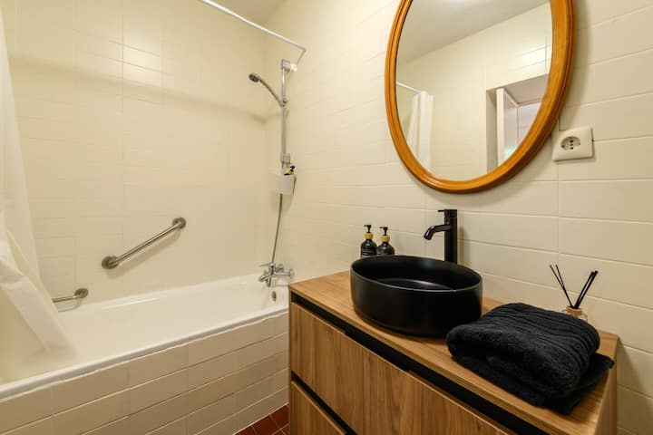 Baño con bañera, lavabo negro sobre encimera de madera y espejo circular: un baño con carácter.