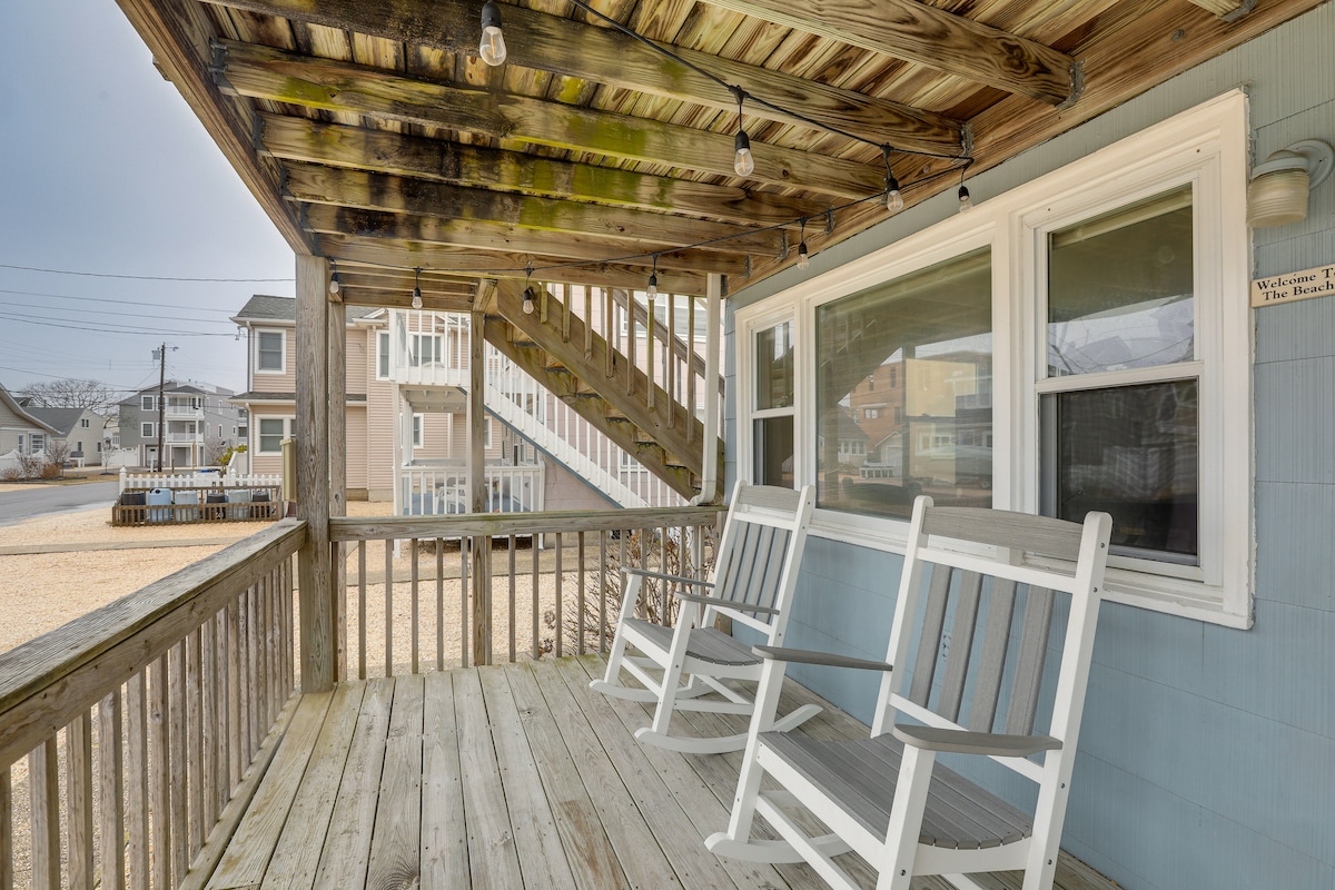 A covered porch is highlighted by two white rocking chairs arranged for relaxation. Above, string lights add a soft ambiance. The porch showcases wooden flooring and staircase leading to the upper level, with a glimpse of the neighborhood beyond.
