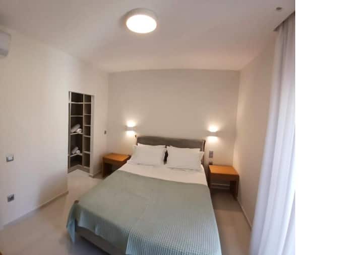 Krásne navrhnutá hlavná spálňa s plyšovou manželskou posteľou, okolitým osvetlením a štýlovými nočnými stolíkmi. Otvorená šatníková skriňa dodáva pohodlie, zatiaľ čo neutrálna farebná paleta a mäkká posteľná bielizeň vytvárajú pokojnú a príjemnú atmosféru pre pokojný spánok.