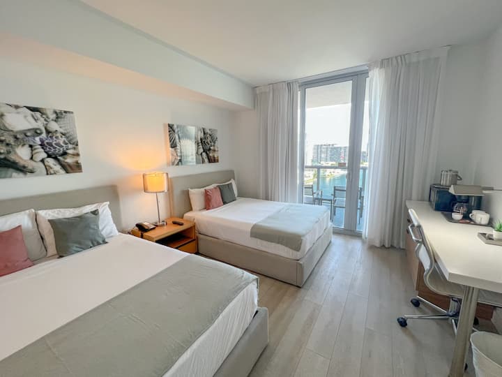 غرفة نوم واسعة مع سرير وتلفزيون بشاشة مسطحة وإضاءة طبيعية ساطعة.