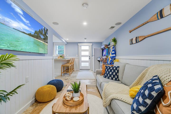 Relájate en la cómoda sala de estar adornada con decoración de temática de playa, colores vibrantes y mucha luz natural para un ambiente sereno y acogedor.