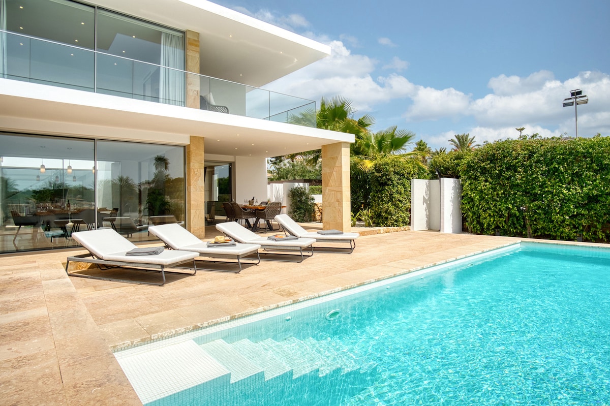 The outdoor area features a private pool with a shallow entry and several lounge chairs arranged nearby. A spacious terrace provides an open view of the pool and surrounding greenery, inviting relaxation and leisure in a sunlit environment.