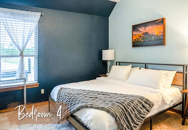 מיטת קווין סייז, מסגרת מתכת מודרנית, קיר מבטא, חלון גדול עם וילונות שקופים, שידות ליד המיטה עם מנורות, יצירות אמנות בנוף