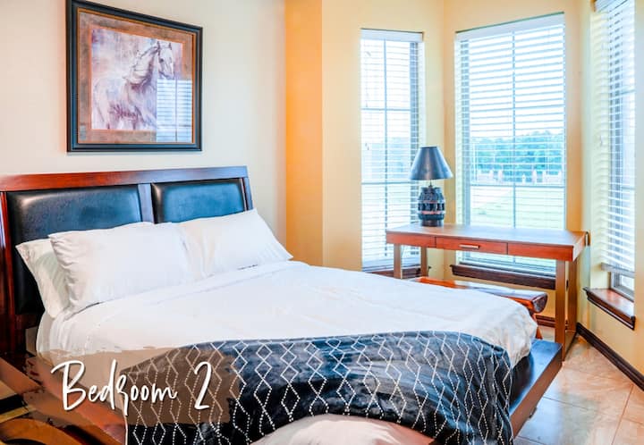 מיטת קווין סייז, מסגרת פלטפורמה מעץ, יחידת מדפים מובנית, חלונות מפרץ עם תריסים, אגרטל דקורטיבי עם צמחים, מנורת שולחן
