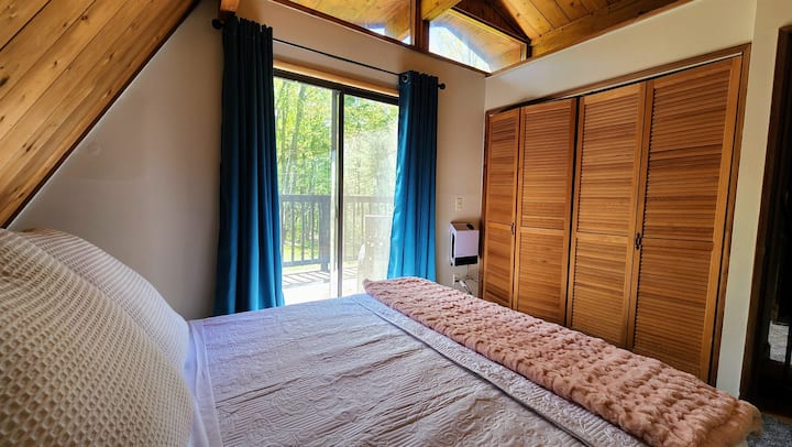 The upstairs bedroom of the Hideaway provides a perfect blend of comfort and convenience. It features a queen-sized bed with a more firm mattress, minimalist decor, and sliding doors that open