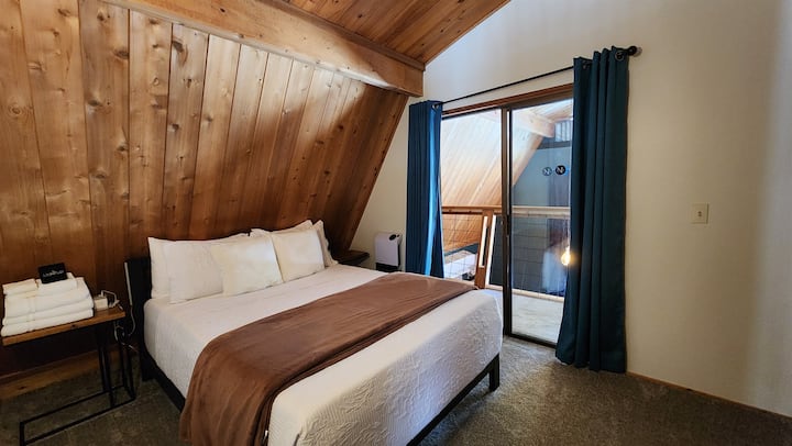 The Hideaway Loft Bedroom is a cozy retreat with a plush queen bed, vaulted ceilings, and the darkest space in the house, perfect for restful nights and peaceful mornings.