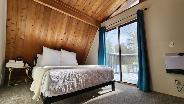 The upstairs bedroom of the Hideaway provides a perfect blend of comfort and convenience. It features a queen-sized bed with a more firm mattress, minimalist decor, and sliding doors that open