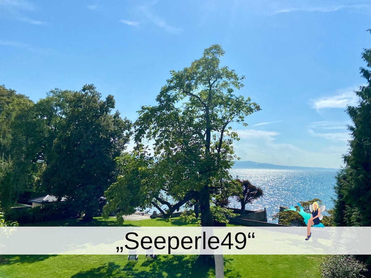 A scenic view of the tranquil Bodensee can be seen from the spacious garden area. Lush trees provide shade, while the shimmering water reflects sunlight, creating a serene atmosphere. The garden is well-maintained, contributing to the peaceful surroundings of the property.