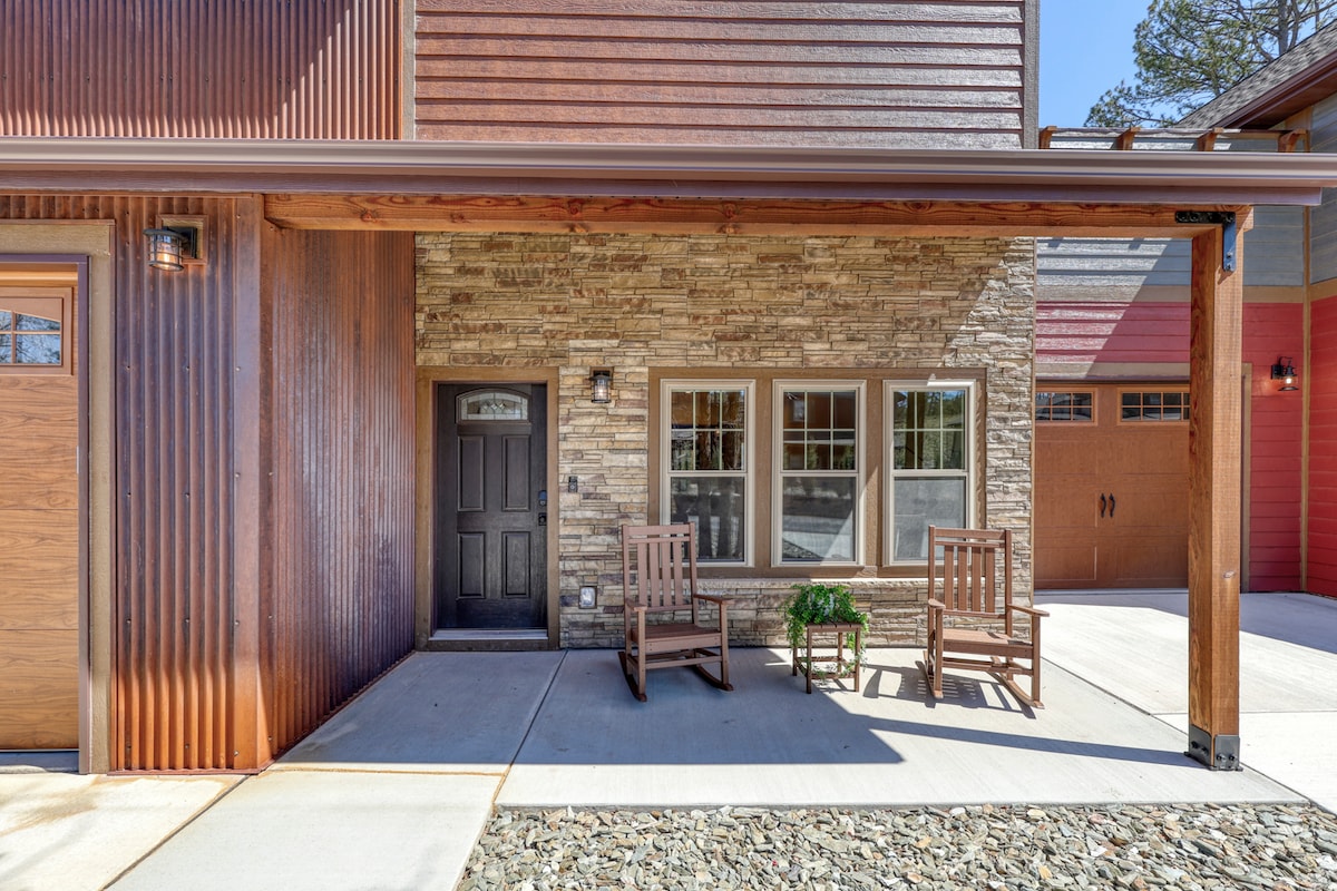 The exterior features a charming facade with a blend of wooden and stone materials. Two welcoming chairs are positioned on the porch, accompanied by a small potted plant. A well-maintained pathway leads to the door, with clear surface parking visible.