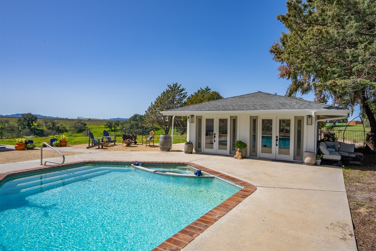 A serene pool area is showcased with a clear blue pool surrounded by a spacious patio. Comfortable outdoor seating and potted plants create an inviting atmosphere. Expansive windows of the casita offer picturesque views of the surrounding countryside.