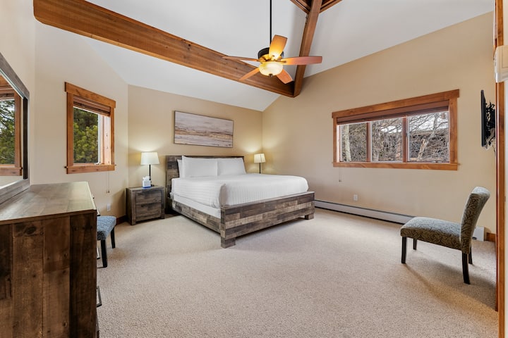 Suite principal con cama tamaño king, techo abovedado, TV de pantalla plana montada, sala de estar, baño privado y vestidor.