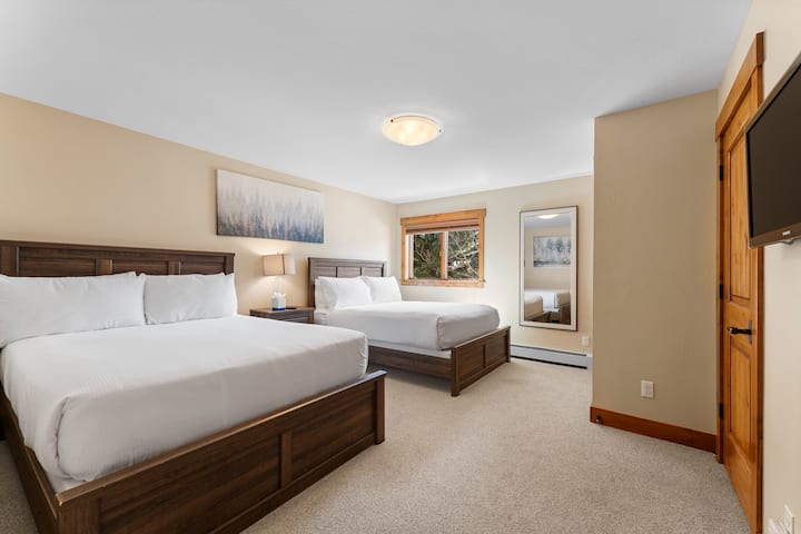 Dormitorio de invitados del segundo nivel superior con dos camas tamaño queen, TV de pantalla plana montado y baño en suite. 