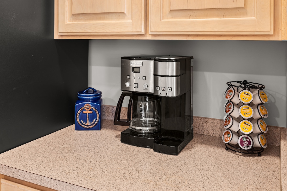 A modern coffee maker is placed on a countertop, next to a carousel of coffee pods. A decorative blue canister featuring an anchor design adds a nautical touch to the space, enhancing the kitchen's functionality.
