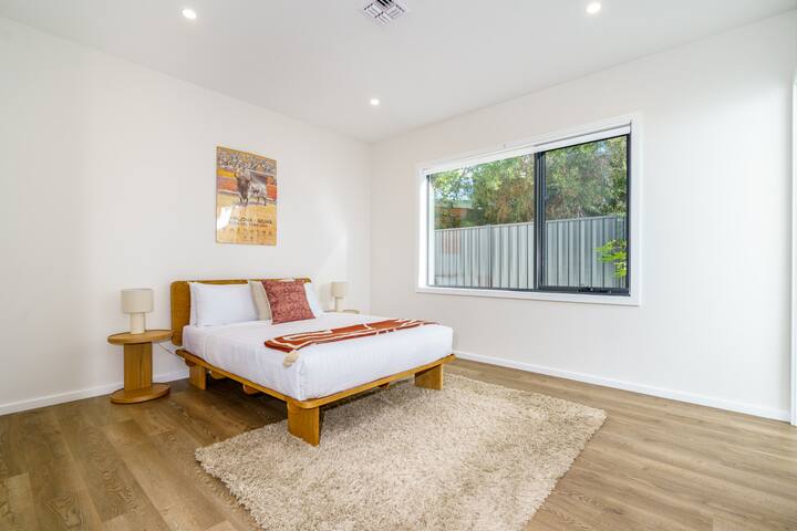 Disfruta de la tranquilidad en este dormitorio luminoso y minimalista con una acogedora cama tamaño queen, una decoración contemporánea y una generosa ventana con vistas al sereno jardín.