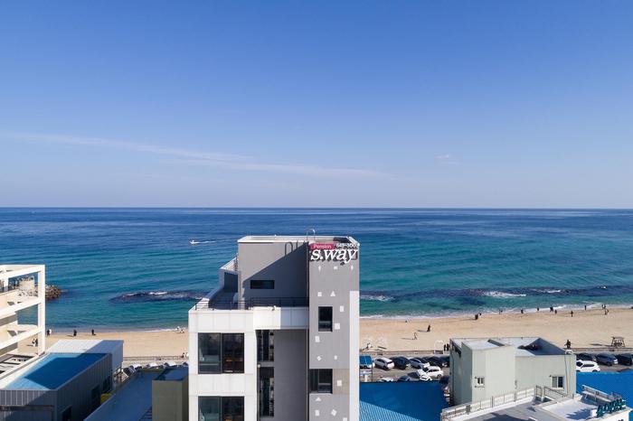 A coastal view is captured, showing the building's exterior with the ocean and sandy beach in the background. The clear blue sky enhances the scene, while the waves gently lap the shoreline, completing the serene atmosphere.