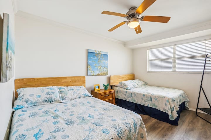 - Dhoma e gjumit e ndritshme ofron dy krevate me madhësi të plotë me shtroja plazhi dhe art simpatik në mur
- Dritarja e gjerë lejon dritën natyrale ndërsa ventilatori i tavanit i mban gjërat të freskëta dhe të freskëta
- Komodina me dekor e bën atë një hapësirë të qetë për të pushuar ose për të lexuar