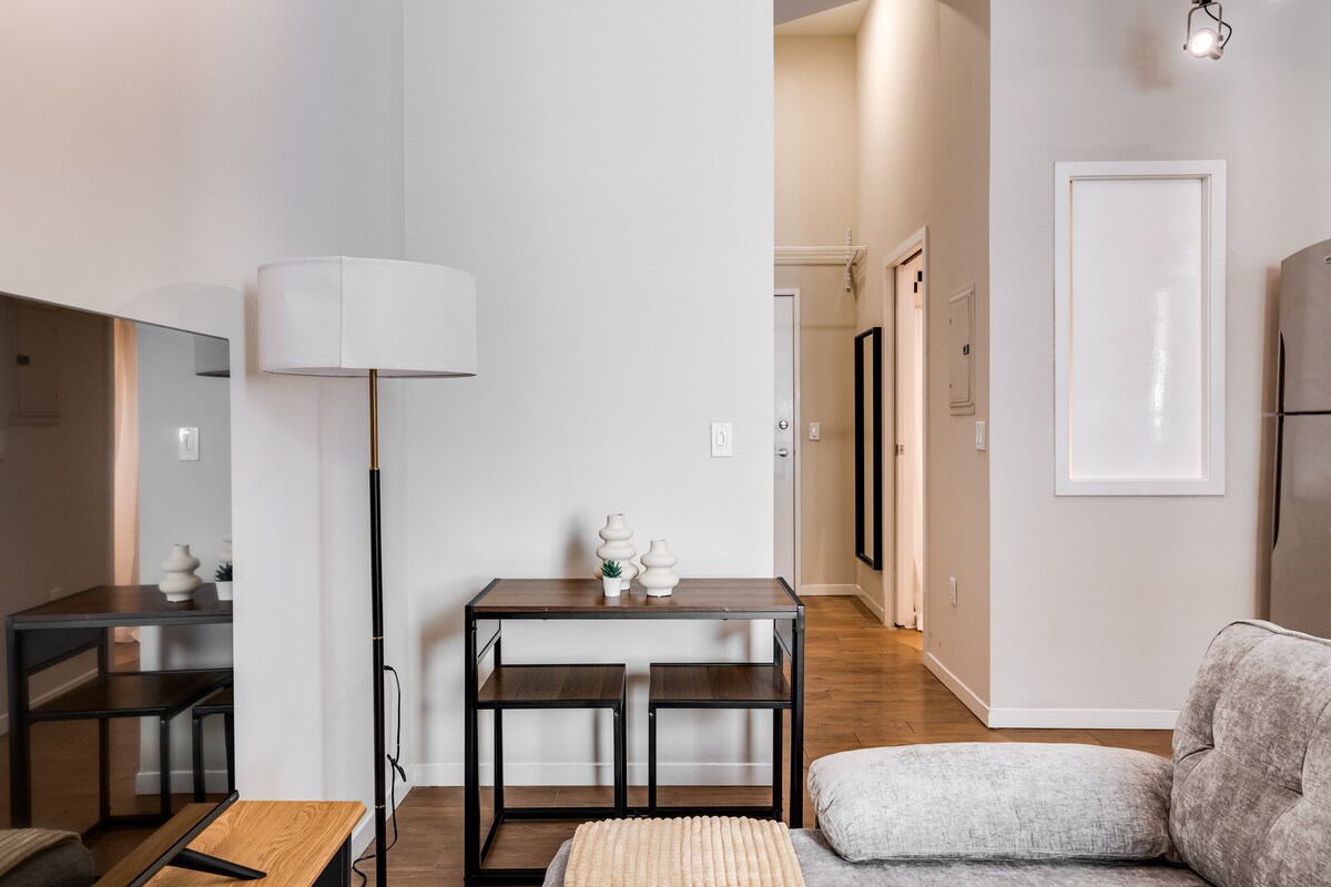 A modern living area showcases a soft sofa beside a sleek coffee table. A lamp stands tall, providing light, while elegant decor items rest on a console table against the wall. The space is brightened by ample natural light flowing in from the open doorway.