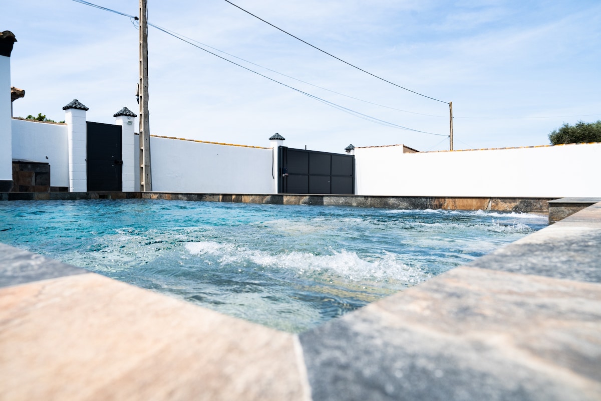 A private pool is featured, surrounded by a stone deck. Clear water is visible, showcasing ripples, while white walls provide a backdrop. The pool area is enclosed by a gate, which is located in the background, ensuring privacy.