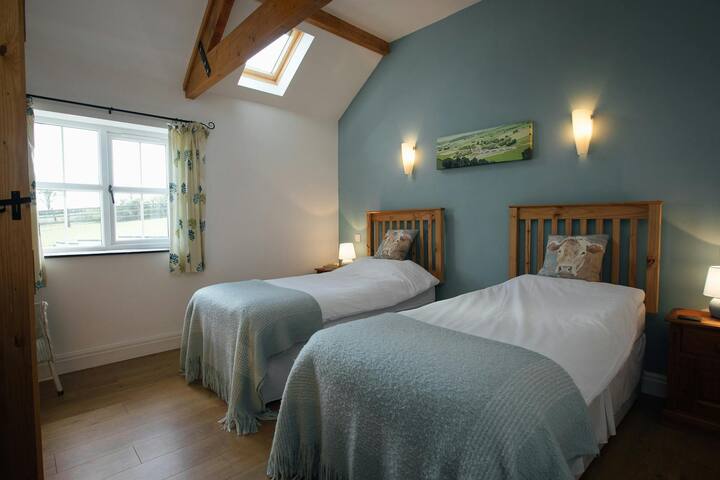 מיטות יחיד זוגיות, ארונות ליד המיטה עם מנורות ונוף כפרי מהחלון