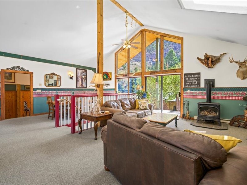 A spacious living area features comfortable leather seating arranged around a central coffee table. Large windows allow natural light to fill the room, highlighting decorative elements like artwork and wooden accents. A cozy fireplace is present, adding warmth to the inviting space.