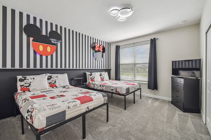 Entrez dans une retraite ludique avec deux lits confortables ornés d'une literie Mickey Mouse vibrante, parfaite pour les familles. Les murs rayés ajoutent une touche amusante, tandis que la grande fenêtre invite la lumière naturelle et offre une vue agréable sur l'extérieur.