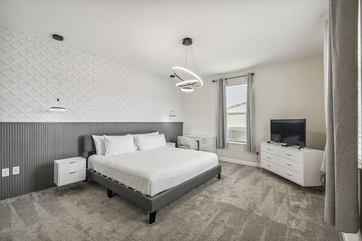 Découvrez une chambre élégante avec un lit gris moelleux et des draps d'un blanc éclatant, des tables de chevet élégantes et un tapis gris doux. De grandes fenêtres remplissent l'espace de lumière naturelle, créant une atmosphère chaleureuse et accueillante pour votre séjour.