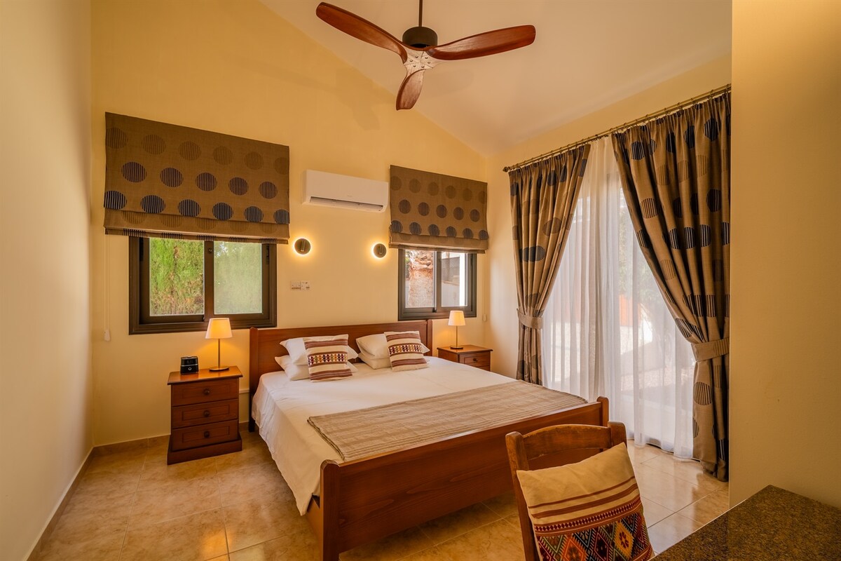 غرفة نوم كينج أولى مع مدخل مباشر إلى الفناء. سرير بحجم كينج، ومروحة سقف، ووحدة تكييف/تدفئة مخصصة، ومنضدة، وخزائن ملابس كبيرة مدمجة، ومكبر صوت بلوتوث/منبه.