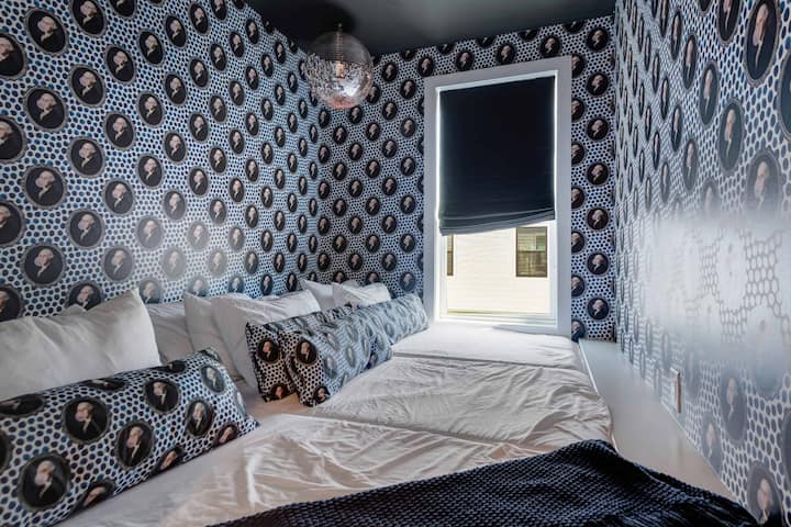 Themed bedroom featuring bold patterned wallpaper, cohesive bedding, and a window with a dark roller shade.
