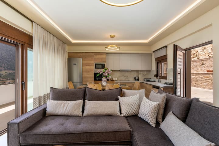 Un coin salon lumineux et ouvert avec un grand canapé d'angle, des coussins superposés et un éclairage chaleureux parfait pour se détendre après une journée de sortie.