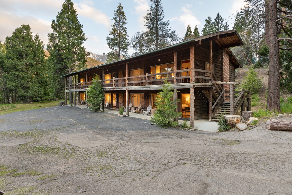 The rustic lodge is presented in a two-story structure surrounded by trees. Each unit features a private porch with seating, inviting relaxation. A spacious paved area in front offers ample parking, and the natural surroundings provide a serene atmosphere.