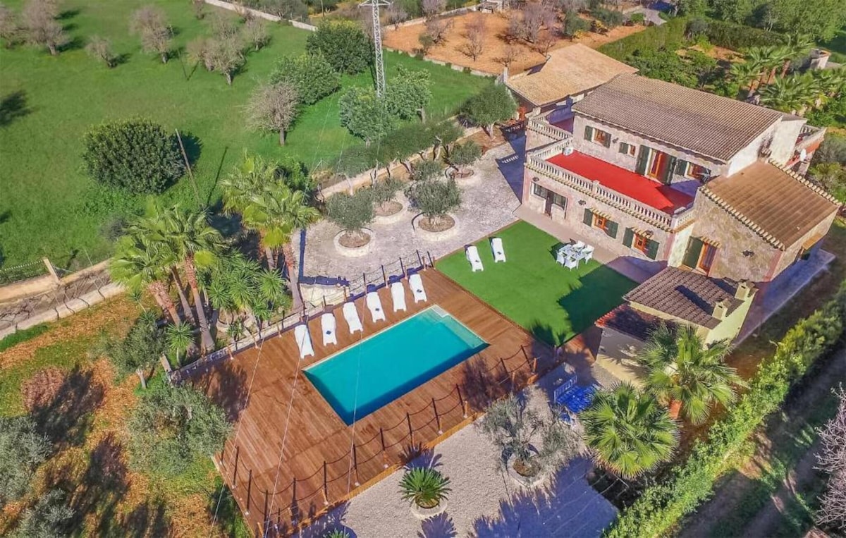 An aerial view of the country house reveals a rectangular pool surrounded by wooden decking and sun loungers. Lush greenery and trees frame the spacious outdoor area, enhancing the sense of privacy. The two-story house features a red-tiled roof and is situated on a tranquil property.